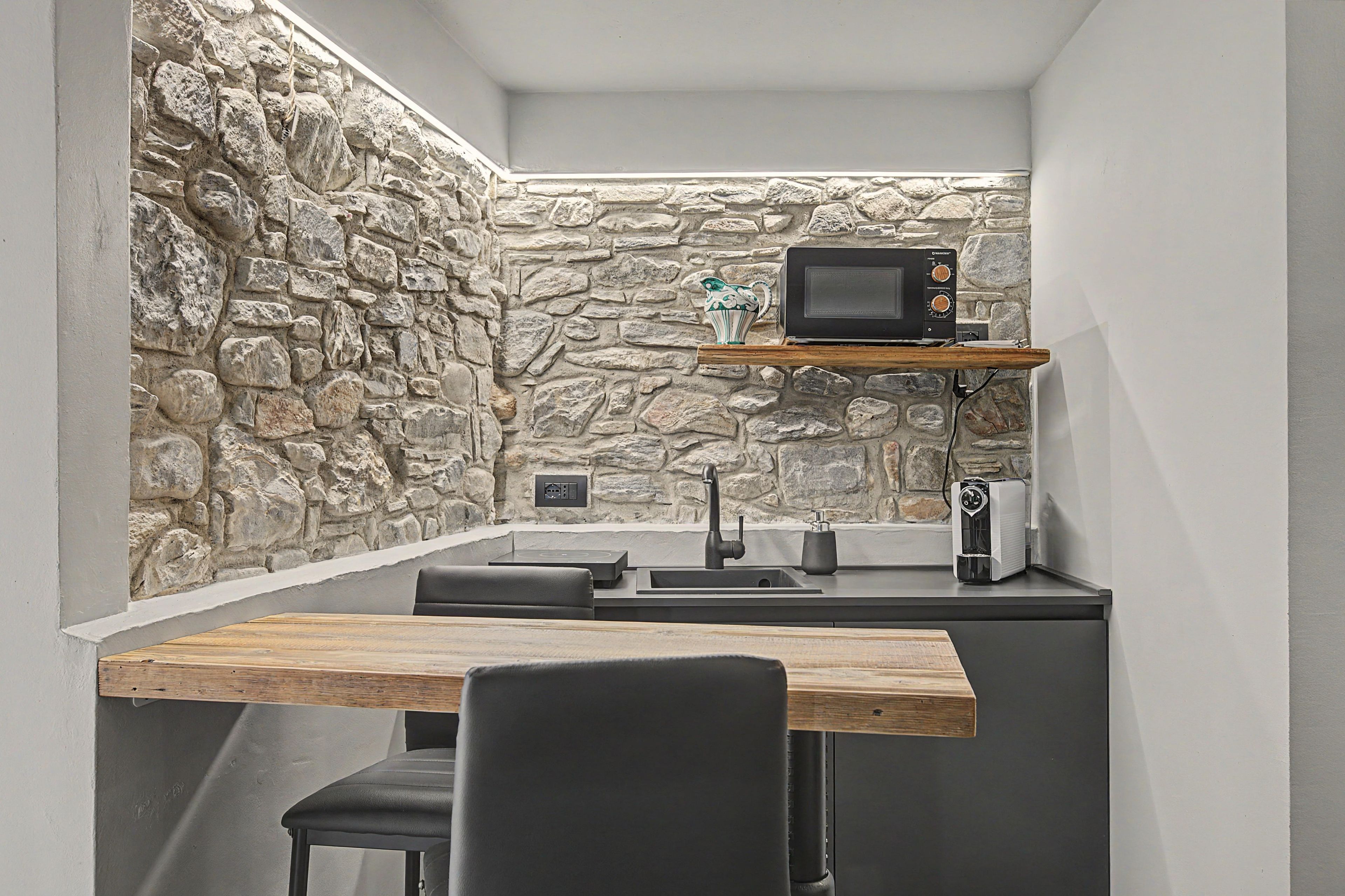 Une cuisine de taille réduite avec un mur en pierre, un four à micro-ondes, une machine à café et un évier.