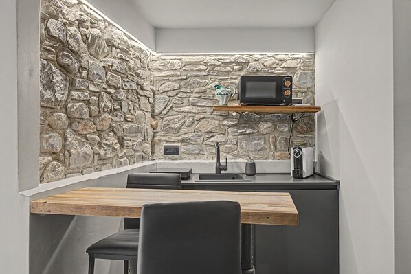 A compact kitchen with a stone wall, a microwave, a coffee maker, and a sink.