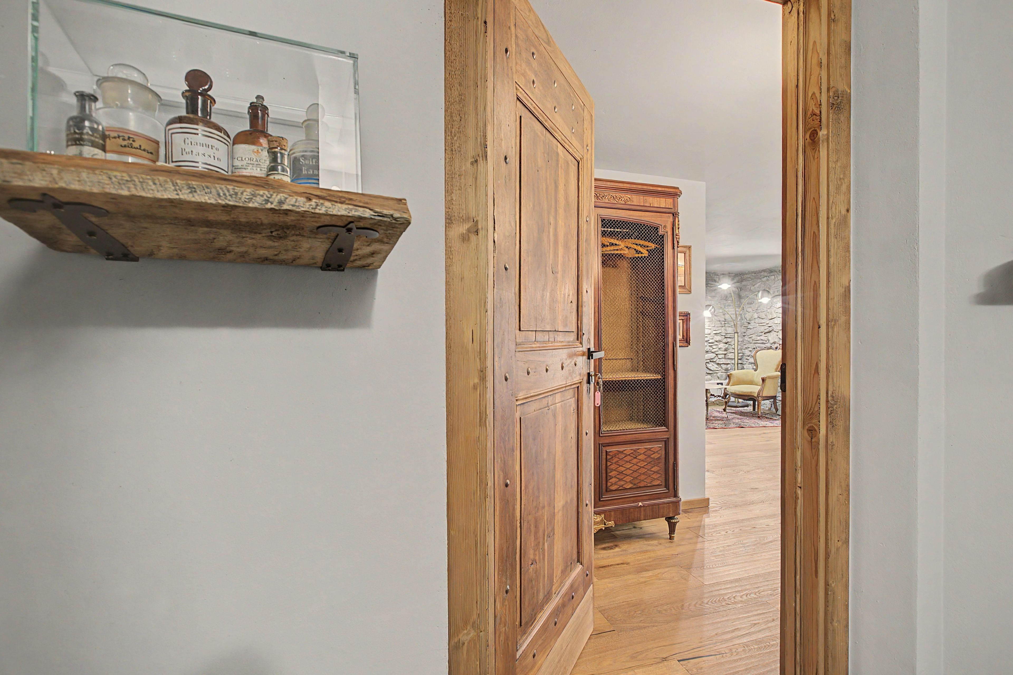A hallway with a wooden cabinet and a glass shelf with bottles.