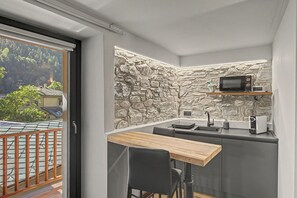 A compact kitchen with a stone wall, a microwave, a sink, and a small table.