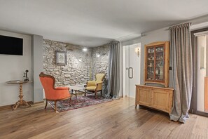 A room with a stone wall, a wooden cabinet, a television, and two chairs.