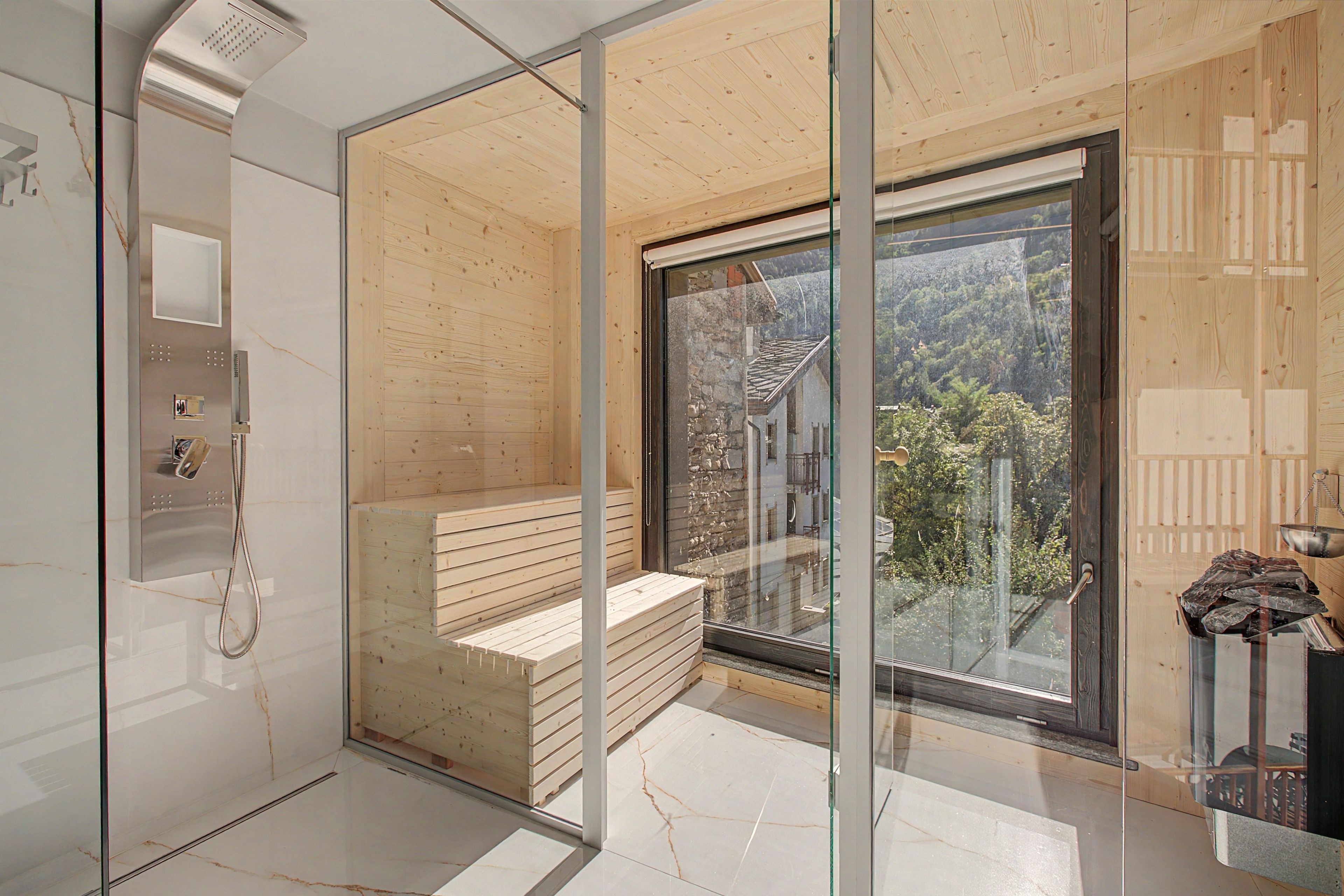 Ein modernes Badezimmer mit Duschkabine aus Glas, einer Holzbank und einem großen Fenster mit Blick ins Freie.