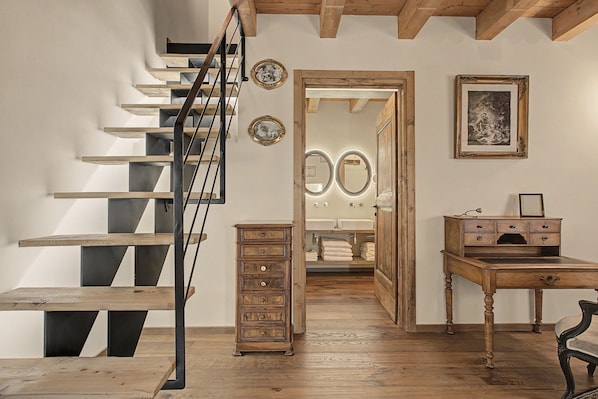 A staircase with a wooden finish and metal railings, leading to a bathroom with a double sink and a mirror.
