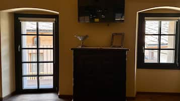 Une pièce dotée d’un plancher en bois, d’une armoire en bois sombre et de deux fenêtres en arc donnant sur un bâtiment à l’extérieur.