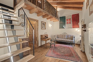 A wooden staircase with a metal railing, a sofa with striped cushions, a patterned rug, and a flag on the wall.