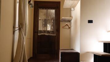 Um corredor com porta de madeira, roupão pendurado, uma mesinha e um banco.