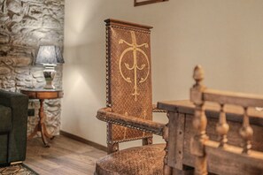 A wooden chair with a cross emblem, a stone wall, and a lamp on a side table.
