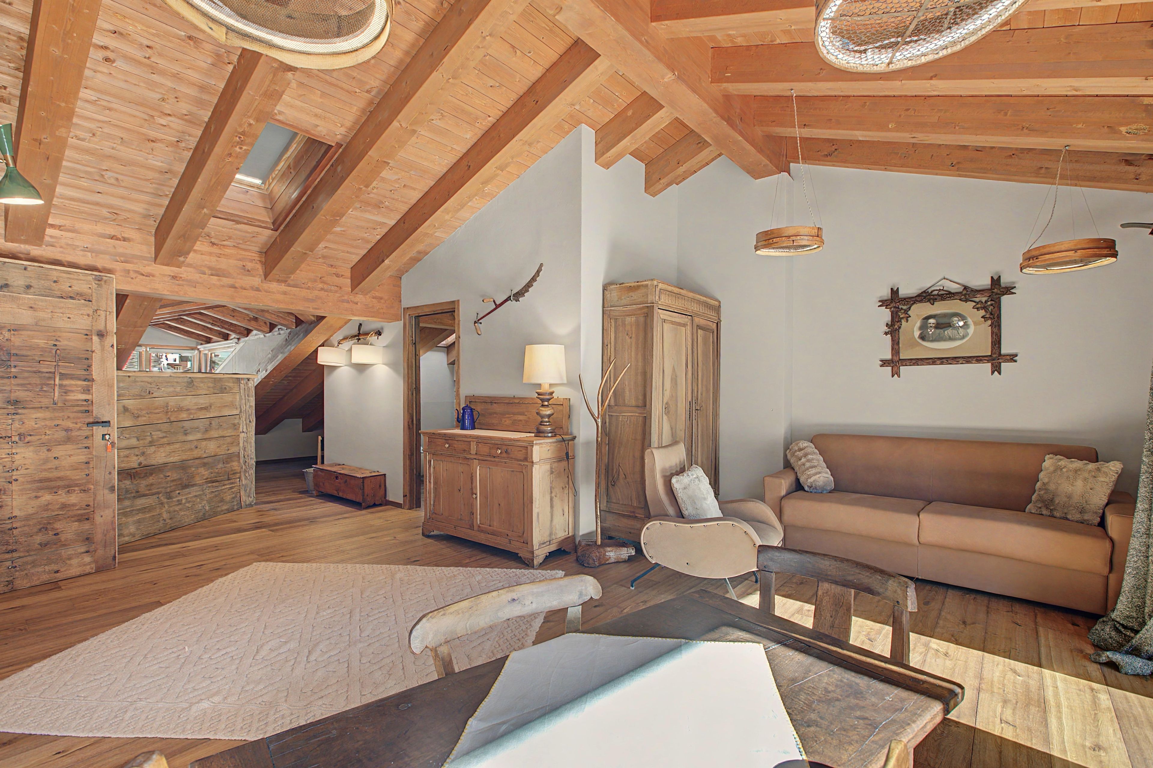 A rustic interior with wooden beams, a wooden cabinet, a sofa, and a dining table.