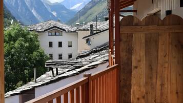 Un balcon doté d’une balustrade en bois, offrant une vue sur un paysage montagneux parsemé de bâtiments traditionnels.