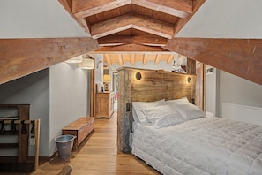 Un dormitorio con cabecera de madera, cama con ropa de cama blanca, un banco de madera y un cubo en el suelo.