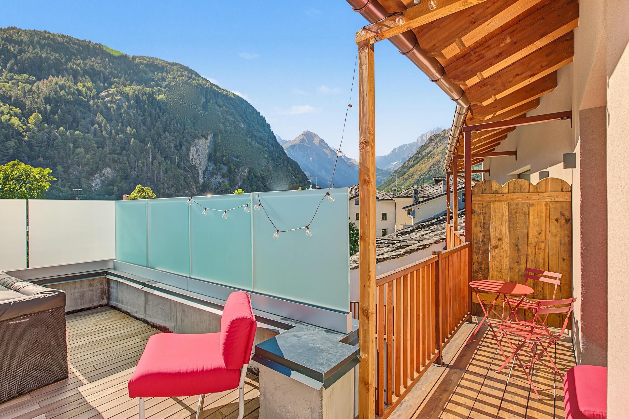 Une terrasse avec vue sur les montagnes, une pergola en bois et des chaises rouges.