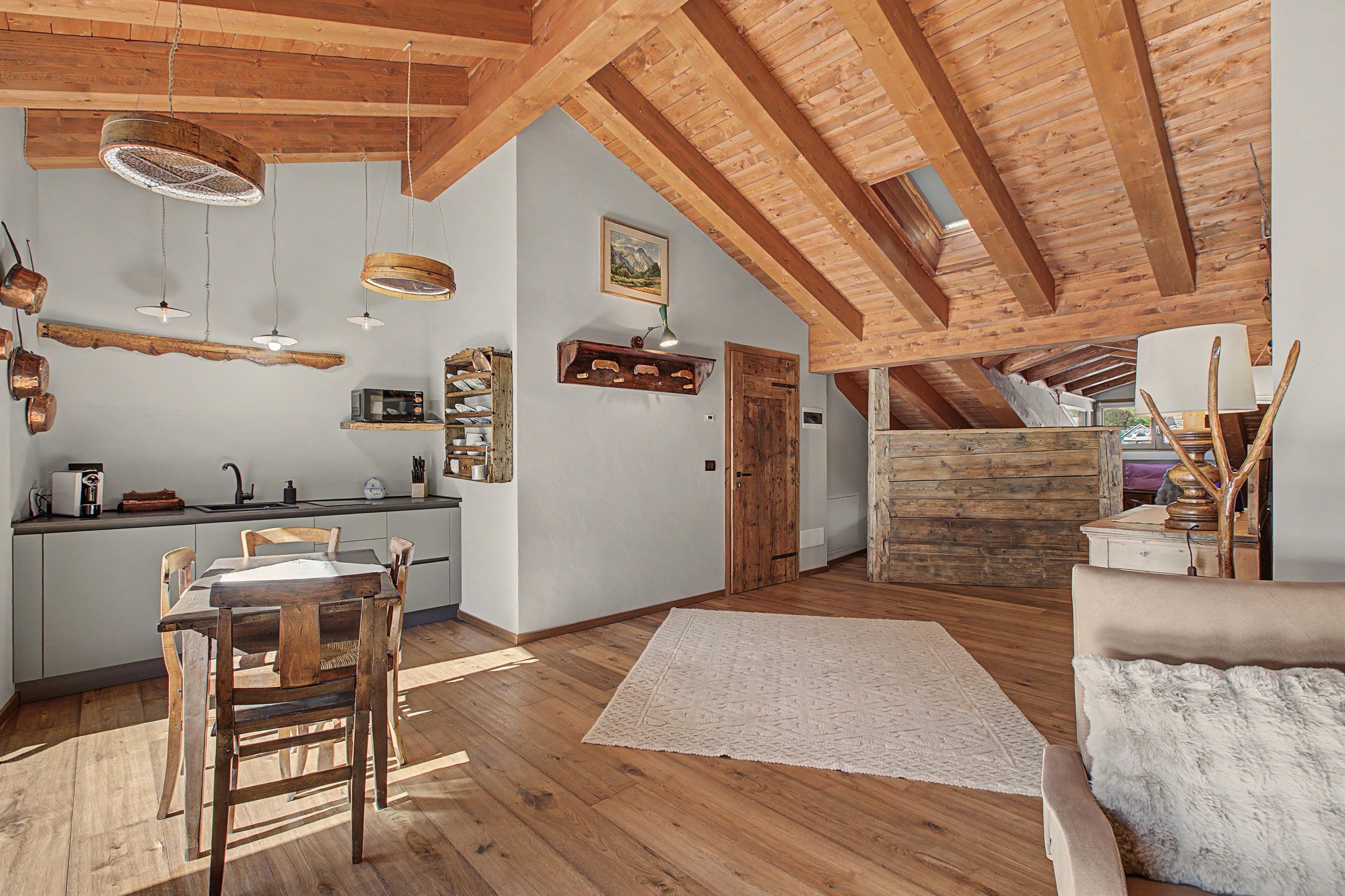 A spacious loft with a high ceiling, exposed wooden beams, a kitchen area with modern appliances, and a cozy seating area with a fluffy rug.