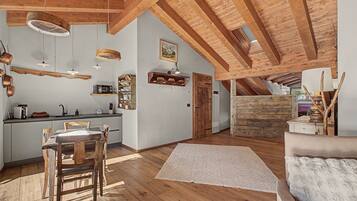 A spacious loft with a high ceiling, exposed wooden beams, a kitchen area with modern appliances, and a cozy seating area with a fluffy rug.