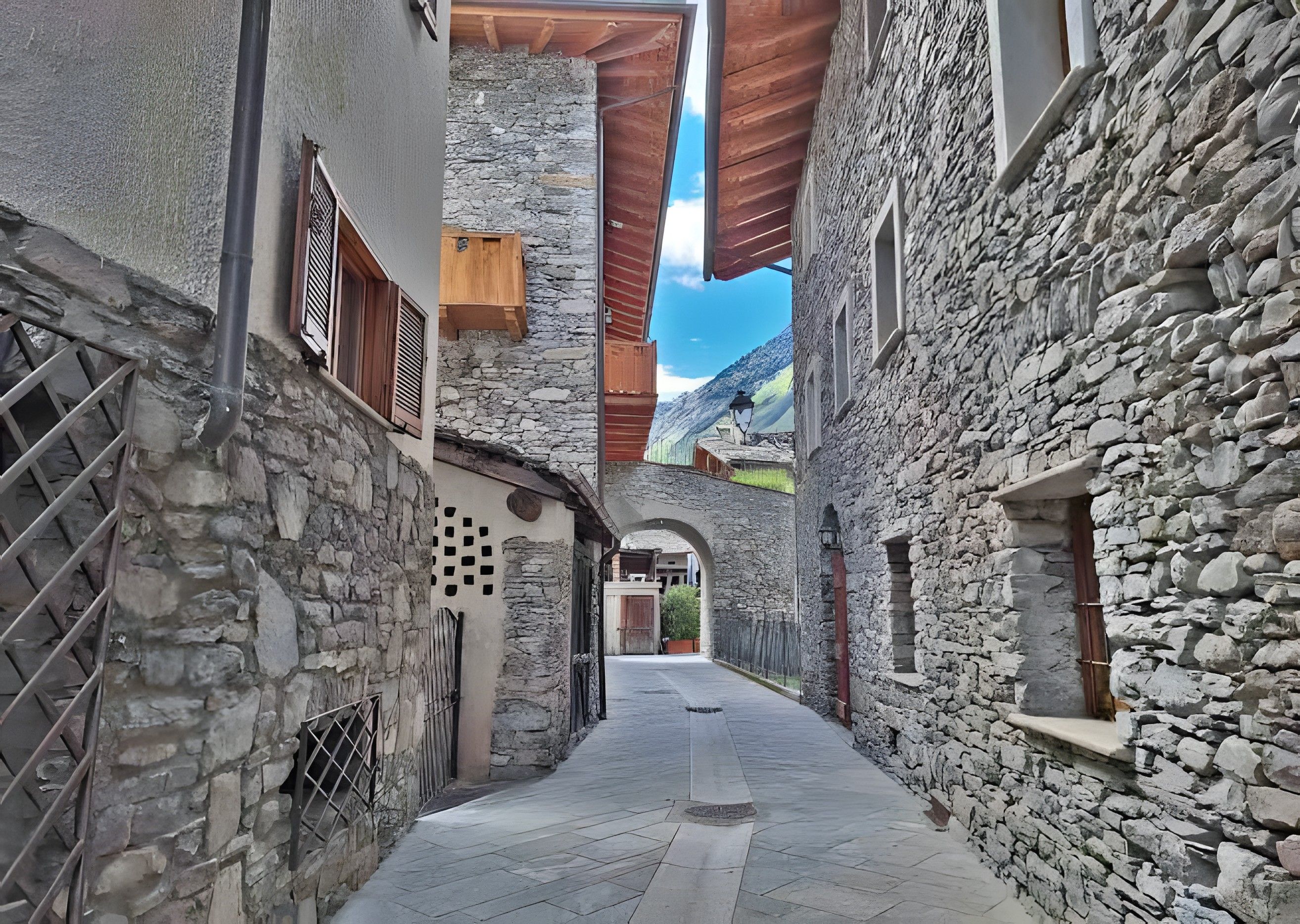 Un étroit sentier pavé de pierres, bordé de bâtiments aux volets en bois et d’un mur de pierres.