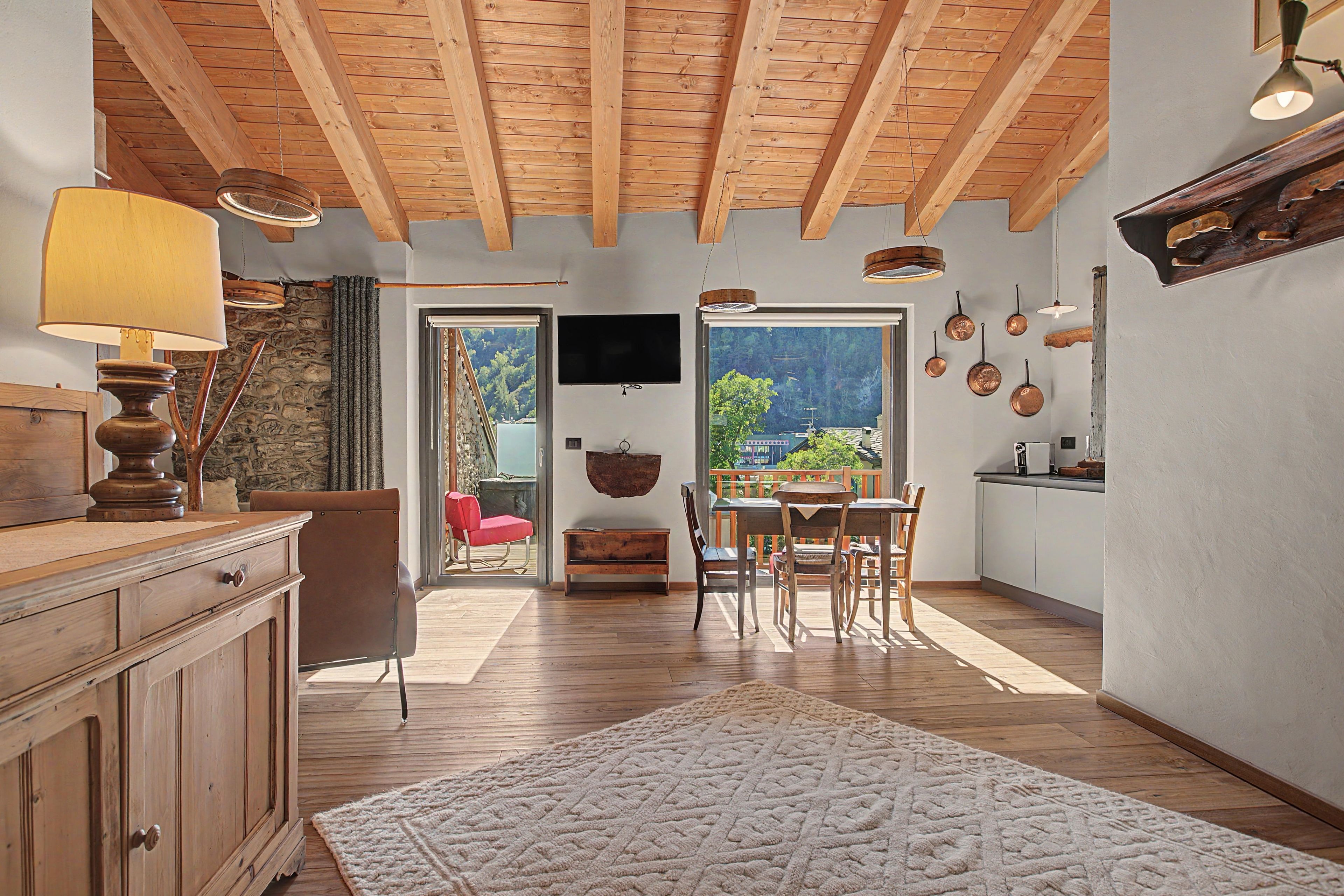 Una cocina amplia con vigas de madera, un comedor con mesa y sillas, y vistas a través de un ventanal.