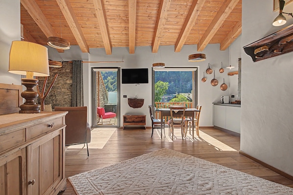 Una cocina amplia con vigas de madera, un comedor con mesa y sillas, y vistas a través de un ventanal.