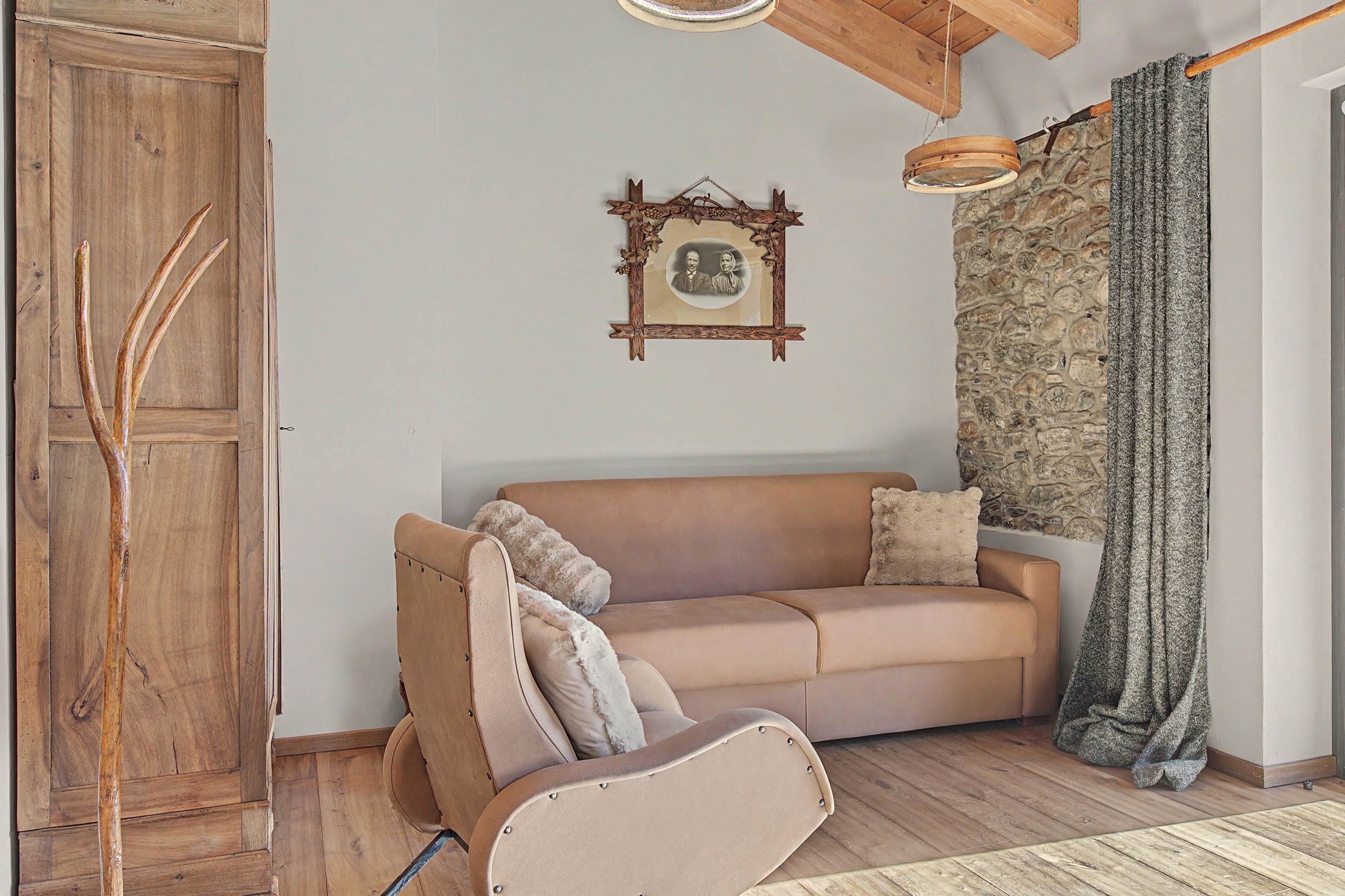 Una habitación acogedora con un armario de madera, un sofá marrón con cojines, una pared de piedra y una lámpara colgante.