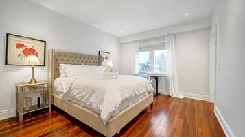 A bedroom with a large bed, a bedside table, a window with curtains, and a framed picture on the wall.