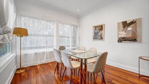 Uma sala de jantar com mesa e cadeiras de vidro, cortinas de renda e obras de arte nas paredes.