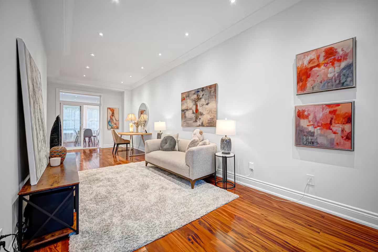A modern living room with hardwood flooring, a grey sofa, a coffee table, and abstract wall art.