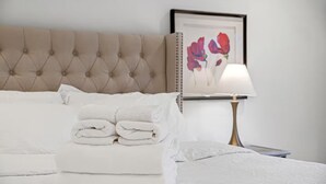 Una cama bien hecha con toallas blancas dobladas, un cabecero capitonado, una mesita de noche con lámpara y un cuadro en la pared.
