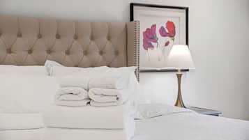 Un lit bien fait, avec des serviettes blanches pliées, une tête de lit capitonnée, une table de chevet avec une lampe et un tableau encadré au mur.