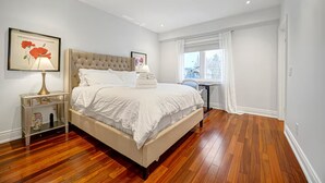 Un dormitorio con una cama grande, una mesita de noche, una ventana con cortinas e imagen enmarcada en la pared.
