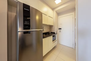 A modern kitchen with stainless steel appliances, white cabinetry, and a tiled floor. - E-side By Bhomy (São Paulo)