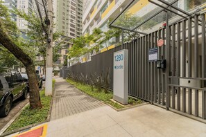 A gated residential area with a pathway, parked cars, and a tall building in the background. - E-side By Bhomy (São Paulo)