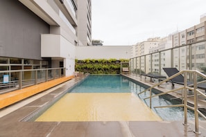 An indoor swimming pool with a tiled deck, lounge chairs, and a glass railing. - E-side By Bhomy (São Paulo)