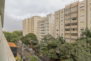 A multi-story residential building with a uniform facade, a street with parked cars, and surrounding greenery. - E-side By Bhomy (São Paulo)