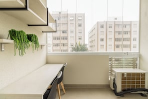A small office space with a white desk, two chairs, a radiator, and a window with a view of high-rise buildings. - E-side By Bhomy (São Paulo)
