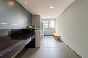 A modern kitchen with a black countertop, a bench, and a window with a view of buildings. - E-side By Bhomy (São Paulo)