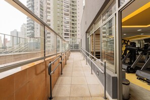 A corridor with a glass railing, leading to a gym area with exercise equipment. - E-side By Bhomy (São Paulo)