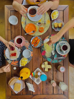 A wooden table with various food items and drinks, including plates with sandwiches, a bowl of fruit, and cups of tea. - Pousada Beija-flor  (Divino de São Lourenço)