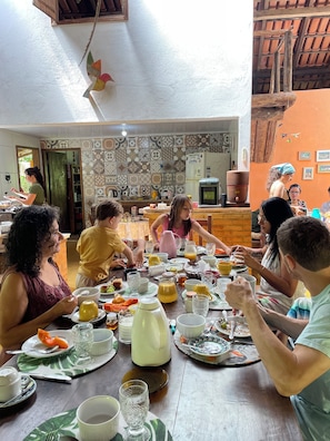 A group of people dining at a wooden table with various dishes and drinks. - Pousada Beija-flor  (Divino de São Lourenço)
