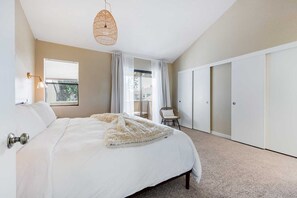 Une chambre avec un grand lit, un luminaire suspendu en osier, une chaise et un placard à portes coulissantes.