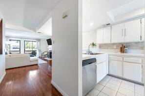 Ein modernes Interieur mit einer Couch, einem Essbereich und einer Küche mit weißen Schränken und einem Geschirrspüler.