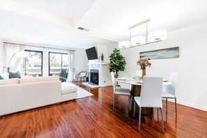 Ein modernes Wohnzimmer mit einer Couch, einem Esstisch, Stühlen, einem Kamin und einem an der Wand befestigten Fernseher.