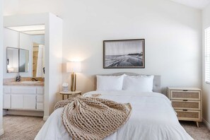 A bedroom with a bed, a bedside table with a lamp, a nightstand, a mirror, and a framed picture on the wall.
