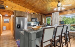A wooden cabin interior with a kitchen, dining area, and a view of the outdoors. - Gee’s Getaway is a cozy mountain retreat nestled in a peaceful setting just minutes from Boone. Relax by the fire, unwind in nature, and enjoy easy access to hiking, dining, shopping, and all the adventures the High Country has to offer. (Boone)