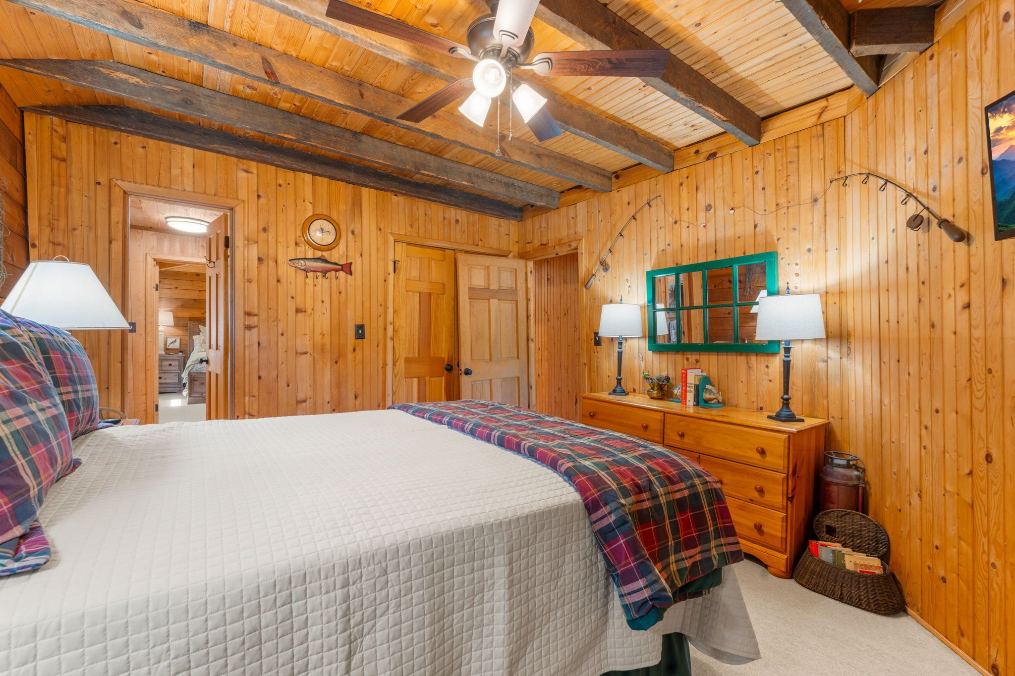 Une chambre à coucher aux murs lambrissés, avec un lit, deux lampes de chevet, une commode et une horloge au mur.