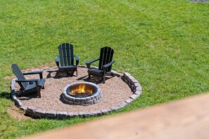A circular fire pit with four Adirondack chairs around it, set on a grassy lawn. - Gee’s Getaway is a cozy mountain retreat nestled in a peaceful setting just minutes from Boone. Relax by the fire, unwind in nature, and enjoy easy access to hiking, dining, shopping, and all the adventures the High Country has to offer. (Boone)