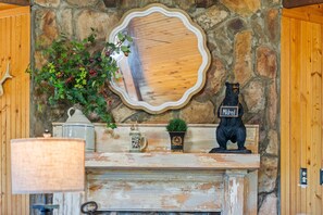 A rustic stone wall with a wooden mirror, a bear statue, and a vase with greenery. - Gee’s Getaway is a cozy mountain retreat nestled in a peaceful setting just minutes from Boone. Relax by the fire, unwind in nature, and enjoy easy access to hiking, dining, shopping, and all the adventures the High Country has to offer. (Boone)