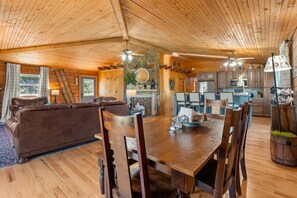 A wooden interior with a dining area, a fireplace, and a kitchen. - Gee’s Getaway is a cozy mountain retreat nestled in a peaceful setting just minutes from Boone. Relax by the fire, unwind in nature, and enjoy easy access to hiking, dining, shopping, and all the adventures the High Country has to offer. (Boone)