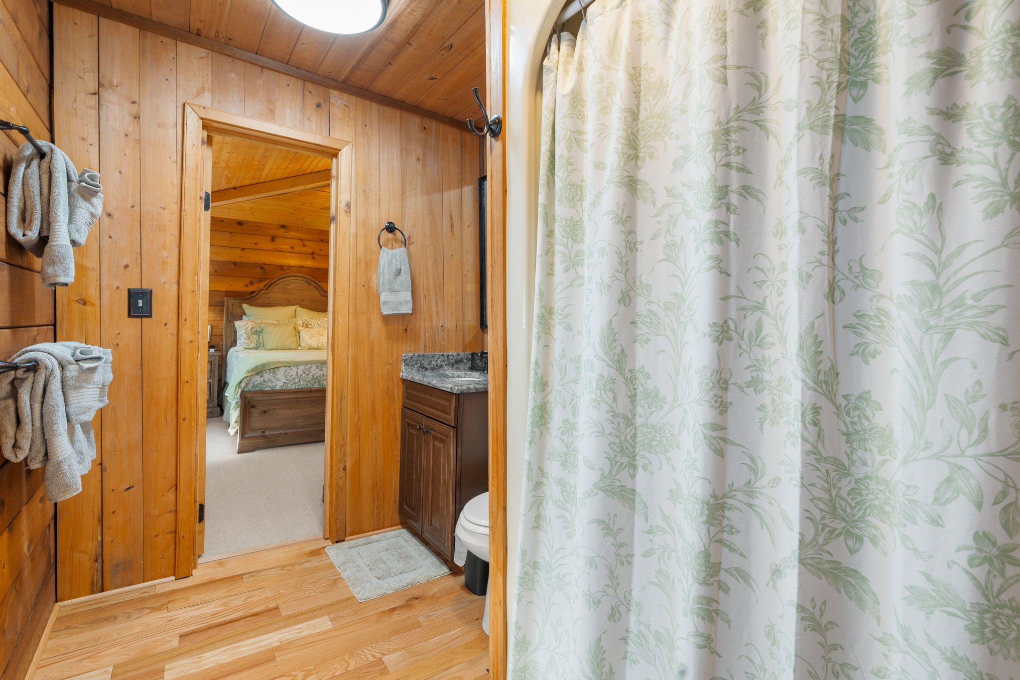 A wooden interior with a bed, a small bathroom, and a door leading to another room.