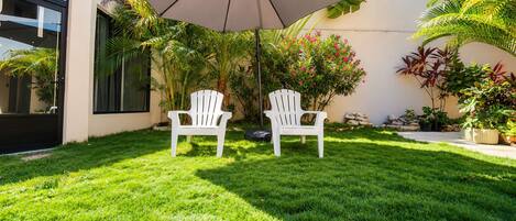 A well-maintained lawn with two white chairs and a large umbrella.