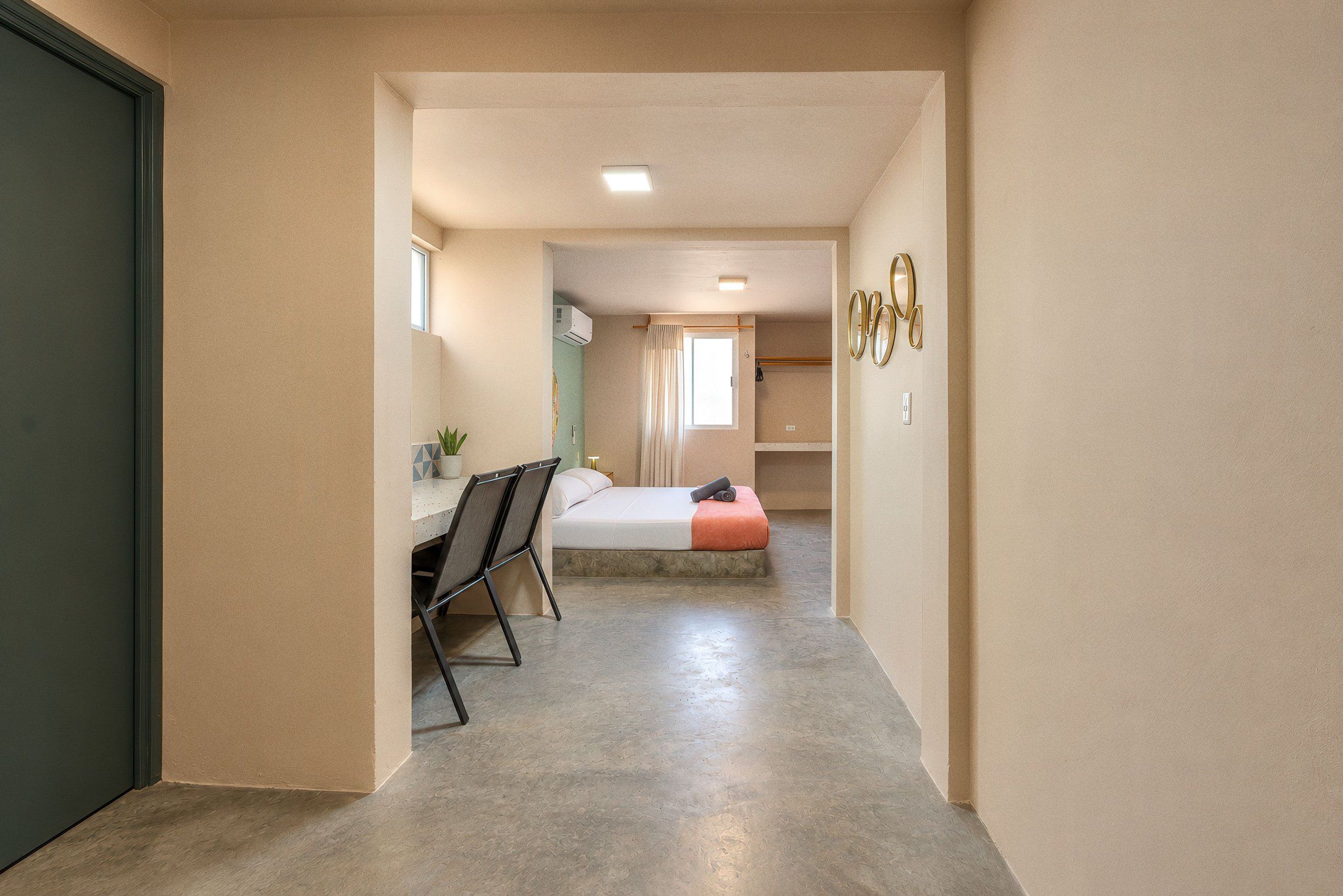 A hallway leading to a bedroom with a bed, a desk, and a chair.