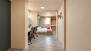A hallway leading to a bedroom with a bed, a desk, and a chair.