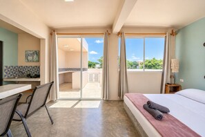 A hotel room with a bed, a desk, a chair, a view of the outside, and a bathroom.